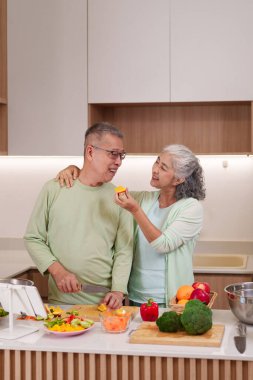 Asyalı yaşlı çift sağlıklı yemek hazırlamaya bayılır. Kadın erkeği portakal dilimiyle besler. Adam sebze doğrar.