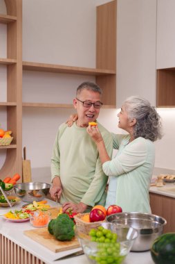 Mutlu Asyalı son sınıf çifti modern mutfaklarında besleyici yemekler hazırlıyor. Onlar taze sebze ve meyve doğrarken hassas bir anı paylaşıyorlar. Sevgi ve ilgi.