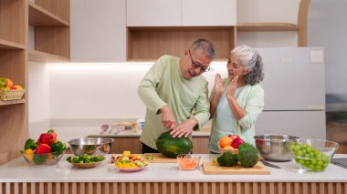 Neşeli Asyalı yaşlılar canlı meyve sebzeleri hazırlıyorlar. Mutluluk ve beraberliği ifade eden modern bir ev mutfağında sağlıklı yemekler yapıyorlar.