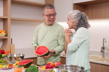 Mutlu yaşlı Asyalı çift taze meyve ve sebze pişirmeyi sever. Onlar parlak modern mutfaklarında tatlı bir anı paylaşıyorlar. Sağlıklı yaşam tarzı.