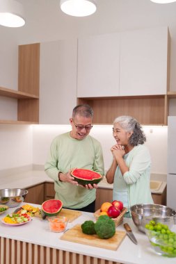 Mutlu Asyalı son sınıf çifti lezzetli taze meyve ve sebze salatası hazırlarken parlak ev mutfağında sağlıklı yemekler pişirirken..