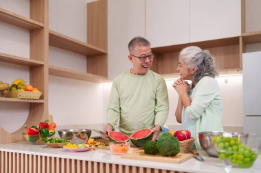 Neşeli Asyalı yaşlı çift besleyici bir yemek için canlı ve sağlıklı malzemeler hazırlıyor. Parlak, çağdaş ev mutfağında birlikte yemek pişirmenin tadını çıkarıyorum..