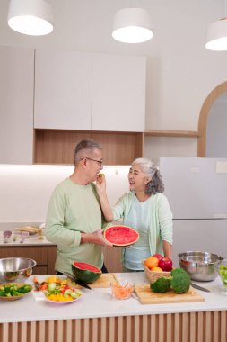 Mutlu Asyalı yaşlı çift birlikte sağlıklı yiyecekler hazırlıyor taze meyve kahkahaları paylaşıyorlar modern mutfak sağlıklı ve neşeli bir yuva sağlıyor.