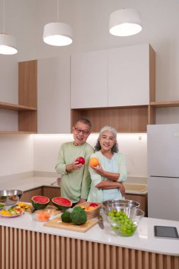 Gülümseyen yaşlı Asyalı kadın taze meyveyi modern mutfakta tutuyor besleyici yemekler hazırlıyor sağlıklı yaşam tarzını ve canlılığını destekliyor.