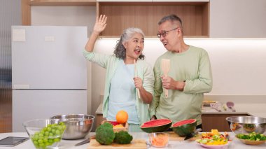 Neşeli Asyalı son sınıf çifti modern mutfakta sağlıklı bir yemek hazırlıyor. Mutlu bir hayatı kutluyorlar taze yemeğin ve birlikte geçirdikleri zamanın tadını çıkarıyorlar..