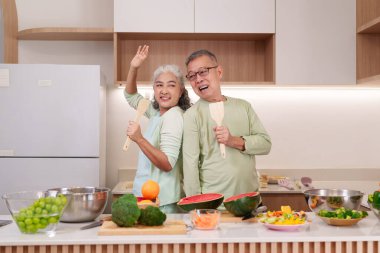 Neşeli Asyalı son sınıf çifti modern mutfaklarında sağlıklı beslenme ve mutluluğu destekleyen taze sebzeler hazırlıyor.