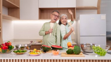 Neşeli Asyalı son sınıf çifti besleyici yemek mutfağı hazırlayın. Mutlu yaşlı yetişkinler taze ürünlerin sağlıklı bir yaşam tarzı yaratmasından hoşlanırlar.