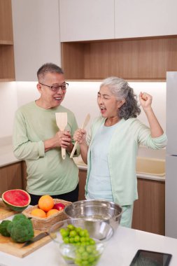 Neşeli Asyalı son sınıf çifti neşeli modern mutfak şarkıları söyleyerek sağlıklı yemek pişirmek için taze malzemeler hazırlıyorlar. Mutlu ev hayatını kutluyoruz..