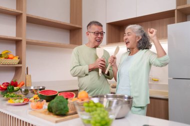 Asyalı yaşlı yetişkinler mutlu bir şekilde taze yemek modern mutfağı hazırlıyorlar. Neşeli emekli çift birlikte gülerek sağlıklı malzemeler pişiriyor..
