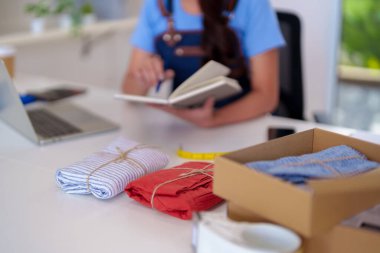 Diligent woman prepares stylish garments for shipping in a home office. She manages online store operations and customer orders.