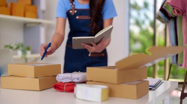 Female entrepreneur diligently prepares garments parcels for shipment. Home based shop operations ensure swift customer delivery.