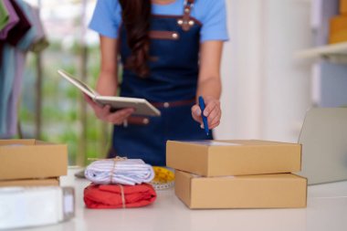 Entrepreneur ships apparel orders from home office. Woman carefully prepares packages for fast customer delivery. Efficient small business operation.