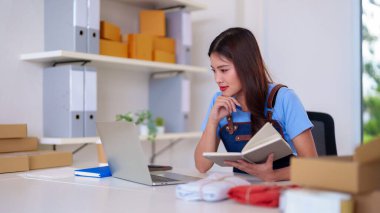 Young Asian entrepreneur diligently fulfilling orders processing shipments managing stock for her successful online retail venture from a comfortable workspace