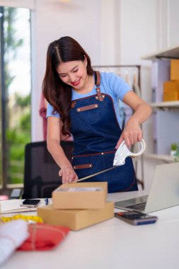 Adult Asian woman preparing customer packages for shipment at her bustling home office managing successful online retail operations