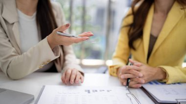 Adult Asian entrepreneurs communicate during a productive meeting analyzing business documents. They share ideas and strategize growth in a modern office setting.