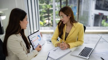 Professional women engage in a productive discussion reviewing charts and statistics. They share insights for successful business development.