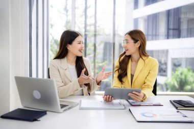 Professional Asian women actively discuss business concepts. They share ideas and strategize for future success in a modern workspace.