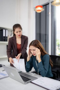 Adult Asian businesswomen experience workplace stress overwhelm. Colleague presents bad news causing anxiety during office meeting. Confrontation at work.