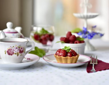 Masada ahududu olan bir fincan kekle (mini tartlar) çay.