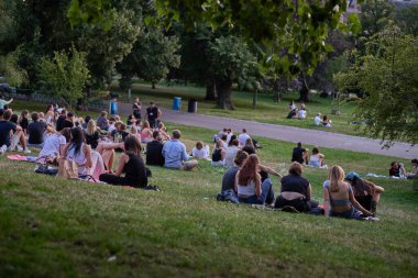 Gençler piknik yapıyor ve 22 Temmuz 2024 'te Çek Cumhuriyeti' nin başkenti Prag 'ın Vinohrady ilçesindeki Riegrovy Sady parkında Prag şehir manzarasının tadını çıkarıyor.