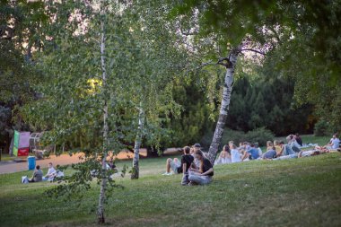 Gençler piknik yapıyor ve 22 Temmuz 2024 'te Çek Cumhuriyeti' nin başkenti Prag 'ın Vinohrady ilçesindeki Riegrovy Sady parkında Prag şehir manzarasının tadını çıkarıyor.