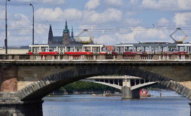 18 Temmuz 2024 'te Çek Cumhuriyeti' nin başkenti Prag sokaklarında toplu taşımacılık, Vltava nehri üzerindeki köprüden geçen eski model kırmızı tramvay.