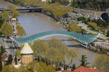 4 Nisan 2025 'te Gürcistan' ın başkenti Tiflis 'teki Kura Mtkvari nehri üzerindeki Barış Köprüsü, çelik ve cam inşaat yaya köprüsünün hava manzarası