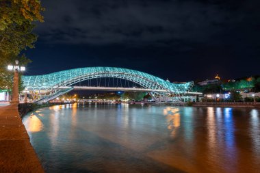 24 Nisan 2025 'te Gürcistan' ın başkenti Tiflis 'te, Kura Mtkvari nehri üzerindeki barış köprüsü, çelik ve cam bina yaya köprüsü gece aydınlandı.