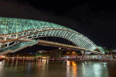 24 Nisan 2025 'te Gürcistan' ın başkenti Tiflis 'te, Kura Mtkvari nehri üzerindeki barış köprüsü, çelik ve cam bina yaya köprüsü gece aydınlandı.