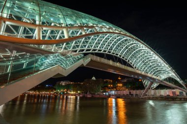 24 Nisan 2025 'te Gürcistan' ın başkenti Tiflis 'te, Kura Mtkvari nehri üzerindeki barış köprüsü, çelik ve cam bina yaya köprüsü gece aydınlandı.