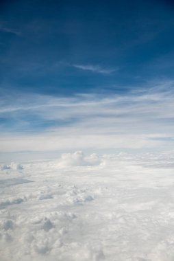 Mavi gökyüzünün altında ince bulutlu, tüylü beyaz bulutlardan oluşan bir uçaktan gelen hava manzarası.
