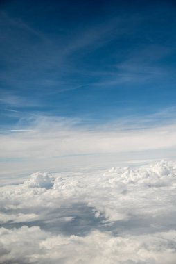 Mavi gökyüzünün altında ince bulutlu, tüylü beyaz bulutlardan oluşan bir uçaktan gelen hava manzarası.