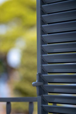 Yeşilliğin bulanık arka planına sahip kısmen açık gri kapı panjurlarının yakın çekim görüntüsü