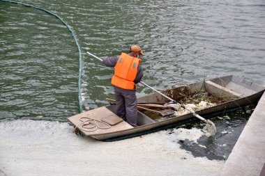 19 Nisan 2024 'te Çin' in orta kesimindeki Pekin 'de Liangma nehrinin sularından dökülen küçük bir tekne enkazı içinde turuncu yelek giyen işçi.