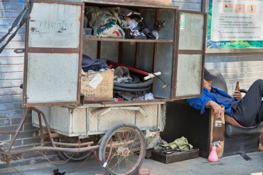 20 Nisan 2024 'te Pekin, Çin' de bir sokakta çeşitli eşyalarla dolu geçici bisiklet tamir arabasının yanında oturan bir adam.
