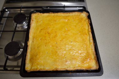 Mutfak tezgahına yerleştirilmiş, arka planında gaz sobası olan, fırında pişirilmiş, geleneksel Gürcü pastası.