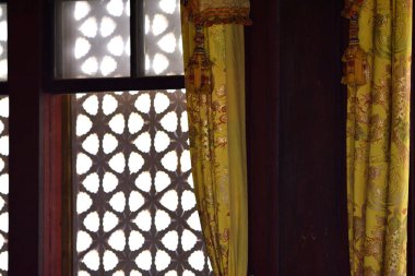 Karmaşık kafes tasarımlı bir pencerenin iç görünümü süslemeli sarı perdeler, yumuşak ışık filtresi