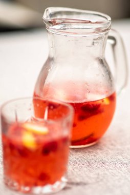 Bir cam sürahi ve kırmızı meyveli içecekle dolu bir bardak.