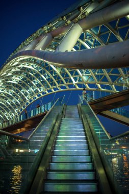 20 Ağustos 2025 'te Gürcistan' ın başkenti Tiflis 'in merkezinde, Kura Mtkvari nehri üzerindeki Barış Köprüsü, çelik ve cam inşaat yaya köprüsünün gece görüşü aydınlatıldı.