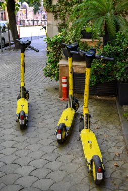 Sarı Yandex elektrikli scooterları 21 Nisan 2025 'te Tiflis, Gürcistan' da bir şehir caddesinde park edilmiş.