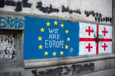 25 Eylül 2025 'te Gürcistan' ın Tiflis kentinde Avrupa entegrasyonuna destek veren AB ve Gürcistan bayrağının yer aldığı bir duvara yazı yazıldı.