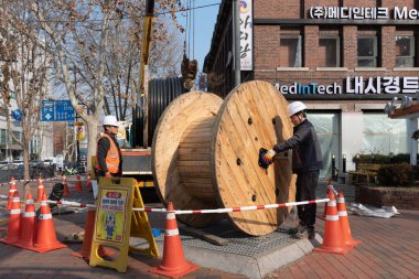 İnşaat işçileri 4 Şubat 2023 'te Güney Kore' nin Seul kentindeki bir caddede büyük ahşap kablo makaralarını taşıyorlar.