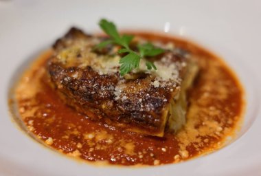 Domates sosuyla servis edilmiş ve maydanozla süslenmiş bir tabak lazanya.