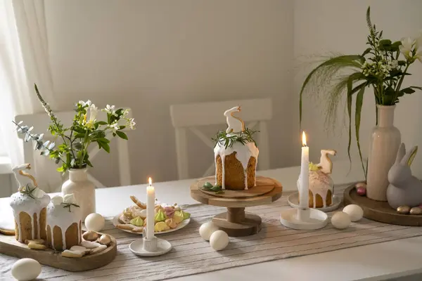 The dining room is decorated for Easter with candles and flowers. Traditional bread kulich, rabbit cookies and eggs.