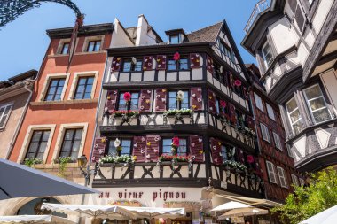 Au Vieux Pignon hediyelik eşya dükkanı. Colmar eski kasaba caddesinde turistler cirit atıyor. Fransa 'nın Colmar şehrinde yarım ahşap renkli Alman evleri alındı. 11 Haziran 2023 'te çekildi.