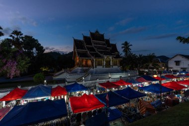 Luang Prabang Ulusal Müzesi 'ndeki Haw Phra Bang tapınağının gece görüşü ve yerel Gece Pazarı. Gün batımında çekilmiş. Luang Prabang, Laos 28 Ekim 2024