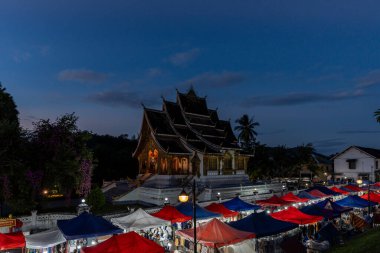 Luang Prabang Ulusal Müzesi 'ndeki Haw Phra Bang tapınağının gece görüşü ve yerel Gece Pazarı. Gün batımında çekilmiş. Luang Prabang, Laos 28 Ekim 2024