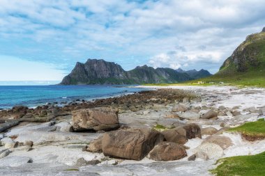 Yazın kayalık kıyı oluşumlarıyla Uttakleiv plajı. Norveç 'in Lofoten adalarındaki ünlü plaj.