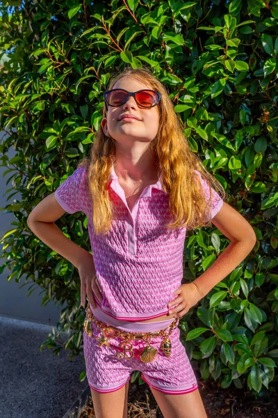 魅力的なモデルバービースタイルの少女は サングラス ピンクのティーシャツ 緑の庭の背景に長い髪のショートパンツ ヴィンテージファッションコンセプトを着ています 高品質の写真 — ストック写真