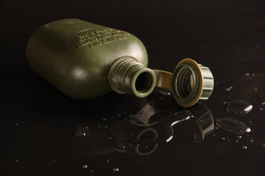 Siyah arka planda yansıması ve su damlacıkları olan küçük plastik ordu yeşili. Mantarı aç. Sırt pozisyonunda.